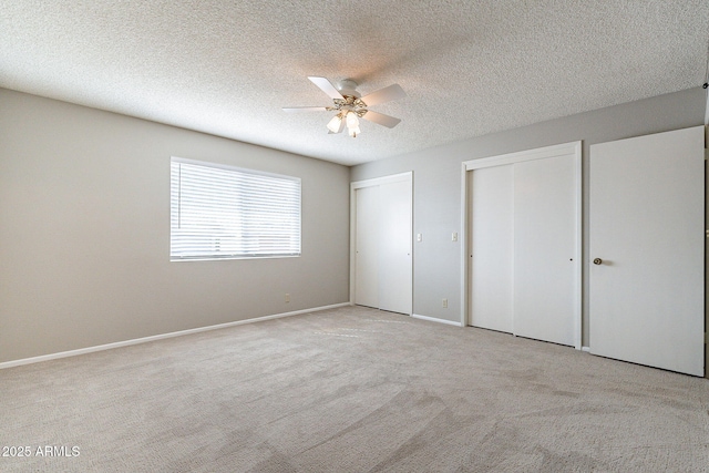 unfurnished bedroom featuring a ceiling fan, baseboards, a textured ceiling, light colored carpet, and two closets