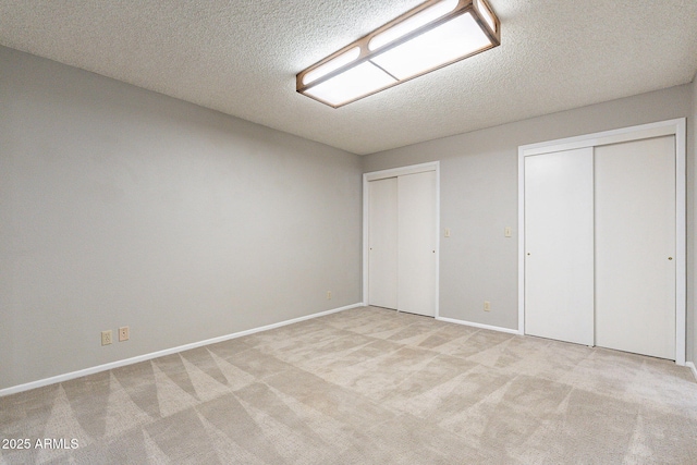 unfurnished bedroom featuring a textured ceiling, light colored carpet, multiple closets, and baseboards