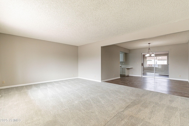 unfurnished living room with a textured ceiling, an inviting chandelier, dark colored carpet, baseboards, and dark wood-style flooring