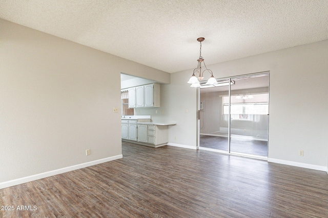 interior space featuring a textured ceiling, dark wood-type flooring, baseboards, and a chandelier