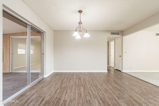 unfurnished room featuring visible vents, a textured ceiling, an inviting chandelier, and wood finished floors