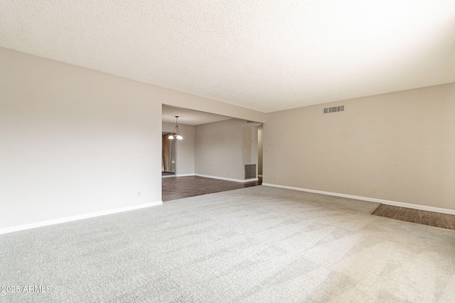 unfurnished room featuring visible vents, baseboards, dark carpet, a notable chandelier, and a textured ceiling