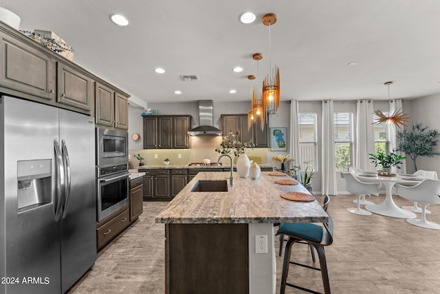 kitchen featuring sink, decorative light fixtures, a center island with sink, wall chimney exhaust hood, and appliances with stainless steel finishes