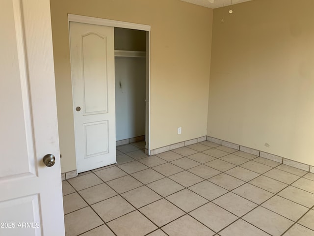 unfurnished bedroom featuring light tile patterned flooring, baseboards, and a closet