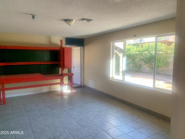 tiled spare room with visible vents, a textured ceiling, and baseboards