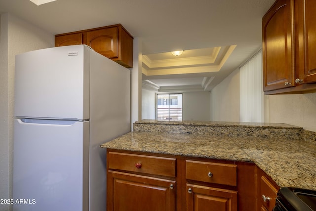 3330 W Danbury Dr Unit E203, Phoenix, AZ 85053 - kitchen with freestanding refrigerator, light stone countertops, a raised ceiling, black range with gas cooktop, and brown cabinets