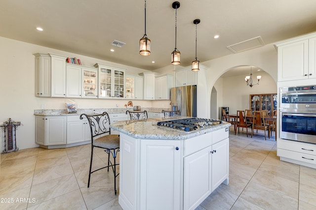 kitchen with visible vents, a kitchen island, arched walkways, stainless steel appliances, and white cabinetry