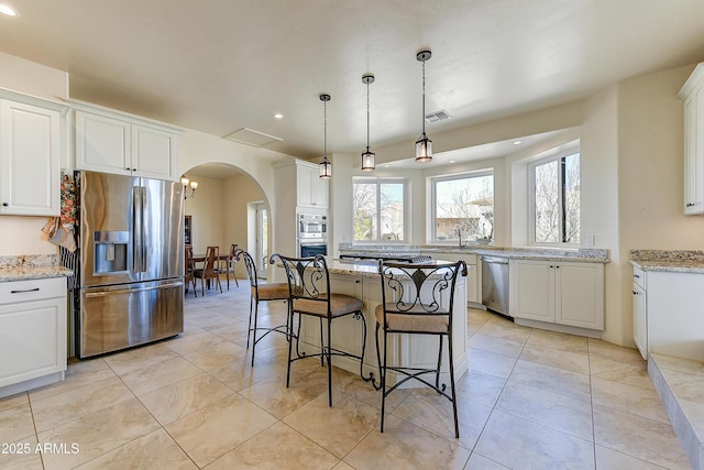 kitchen featuring visible vents, a kitchen breakfast bar, stainless steel appliances, arched walkways, and white cabinets