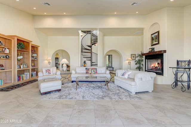 living room with visible vents, a multi sided fireplace, stairs, a high ceiling, and arched walkways