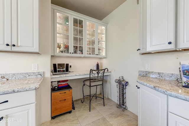 kitchen featuring light stone counters, white cabinetry, and glass insert cabinets