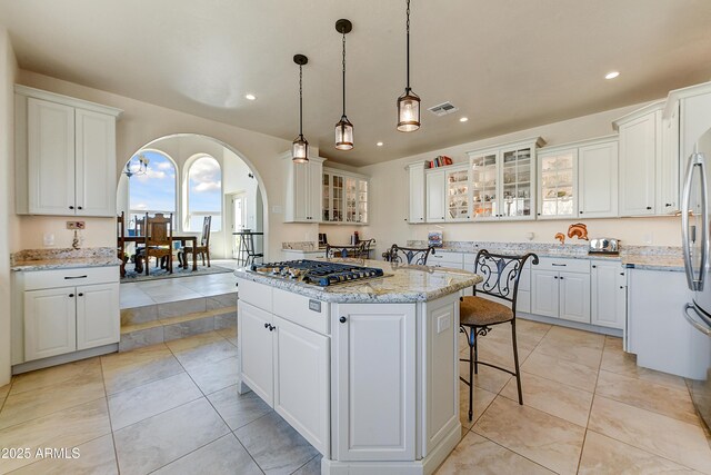 kitchen with visible vents, a kitchen island, stainless steel gas stovetop, arched walkways, and white cabinets