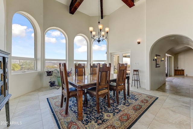 dining space with beam ceiling, a towering ceiling, arched walkways, light tile patterned flooring, and a chandelier