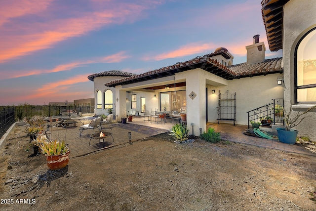 back of property at dusk with fence, stucco siding, a fire pit, a tiled roof, and a patio area