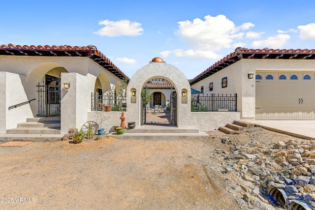 mediterranean / spanish-style house with a fenced front yard, a tile roof, stucco siding, a garage, and a gate