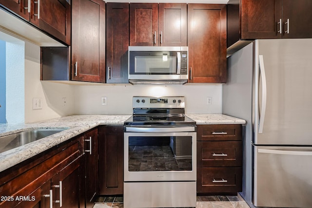 kitchen featuring dark brown cabinetry, stone finish floor, appliances with stainless steel finishes, light stone counters, and a sink