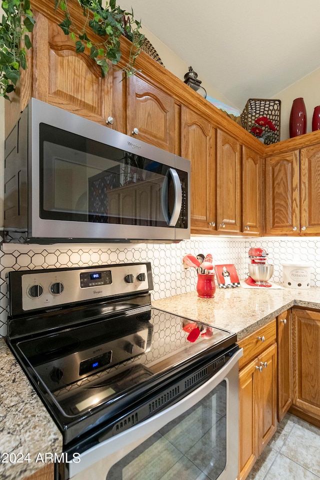 kitchen with appliances with stainless steel finishes, light stone countertops, decorative backsplash, and light tile patterned floors