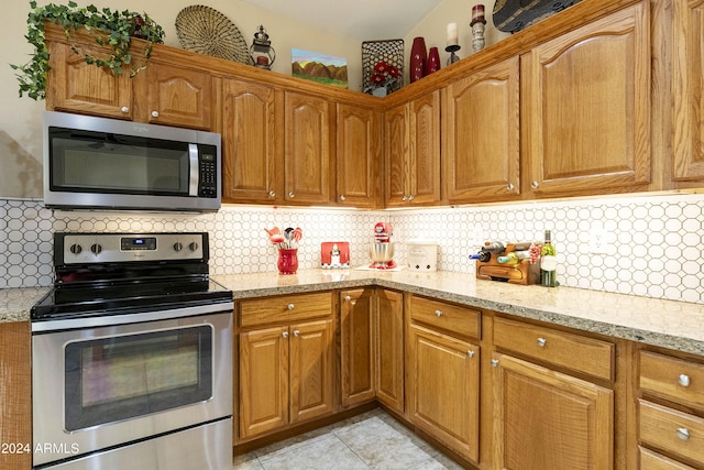 kitchen with appliances with stainless steel finishes, light tile patterned floors, tasteful backsplash, and light stone countertops