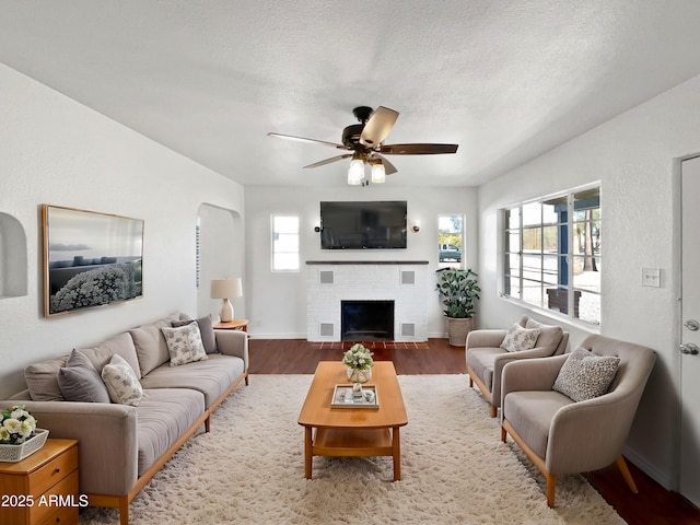 living room featuring wood-type flooring, ceiling fan, a fireplace, and a textured ceiling