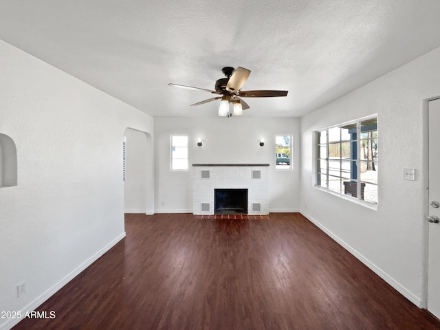 unfurnished living room featuring a fireplace, dark wood-type flooring, a healthy amount of sunlight, and ceiling fan