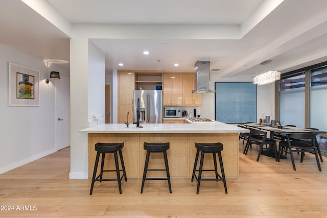 kitchen featuring wall chimney range hood, kitchen peninsula, a breakfast bar area, light hardwood / wood-style floors, and stainless steel appliances