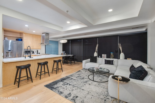 living room featuring beamed ceiling, sink, a tray ceiling, and light wood-type flooring