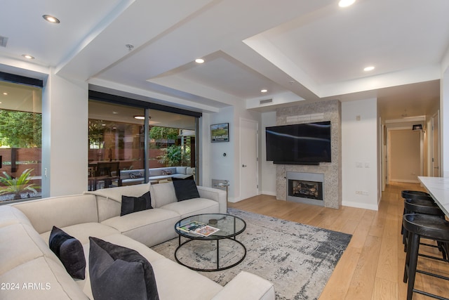 living room featuring light hardwood / wood-style flooring, a tray ceiling, and a fireplace