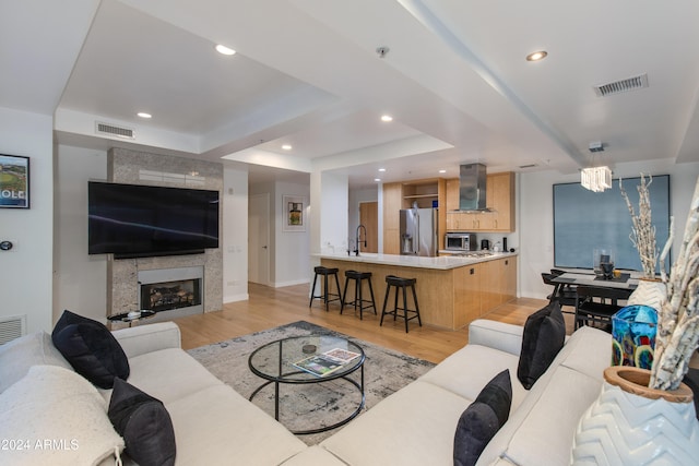 living room featuring sink, a tiled fireplace, light wood-type flooring, and a raised ceiling