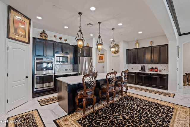 kitchen featuring a breakfast bar, a center island with sink, hanging light fixtures, tasteful backsplash, and stainless steel appliances