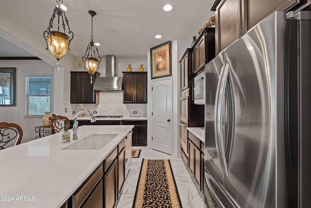 kitchen featuring decorative backsplash, appliances with stainless steel finishes, sink, wall chimney range hood, and decorative light fixtures