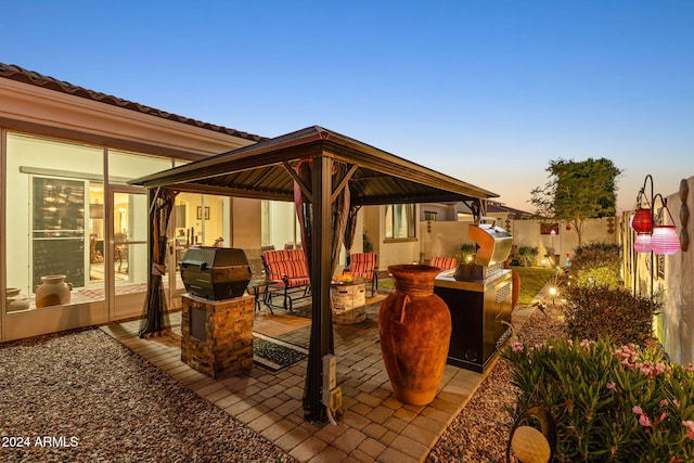 patio terrace at dusk with a gazebo, an outdoor kitchen, and area for grilling