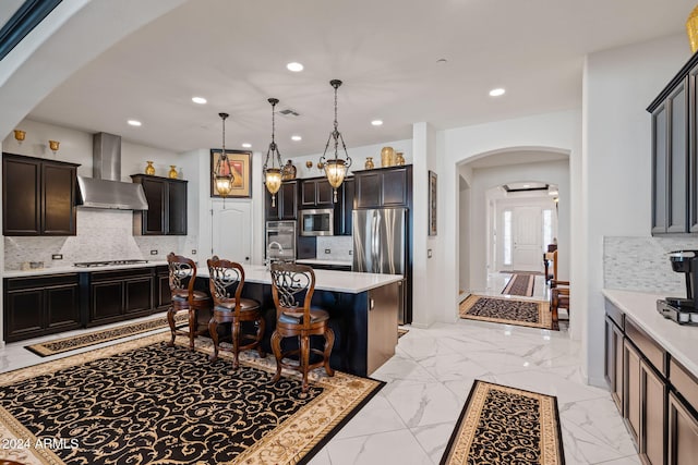 kitchen with tasteful backsplash, stainless steel appliances, a center island with sink, and wall chimney exhaust hood