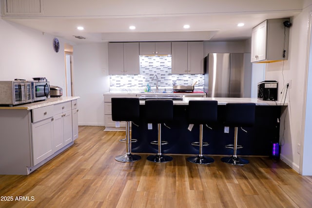 kitchen featuring gray cabinetry, sink, light hardwood / wood-style flooring, appliances with stainless steel finishes, and a kitchen bar