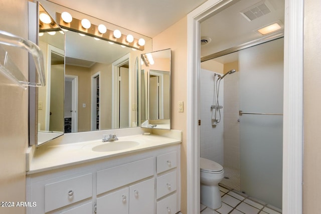 bathroom with toilet, vanity, a tile shower, and tile patterned flooring