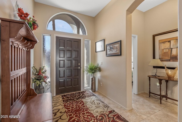 entryway with a towering ceiling, baseboards, arched walkways, and light tile patterned flooring