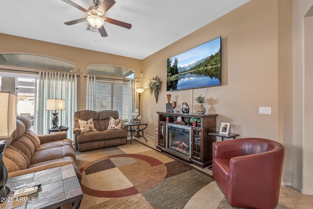 living room with ceiling fan, visible vents, baseboards, and a glass covered fireplace