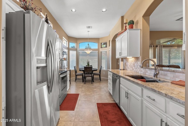 kitchen featuring appliances with stainless steel finishes, a sink, white cabinetry, pendant lighting, and backsplash