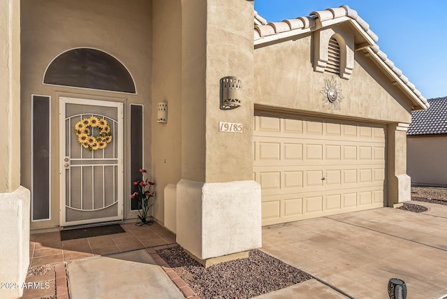 property entrance with a garage, a tiled roof, driveway, and stucco siding