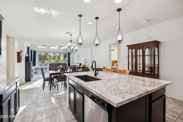 kitchen featuring an island with sink, sink, hanging light fixtures, stainless steel dishwasher, and light stone counters