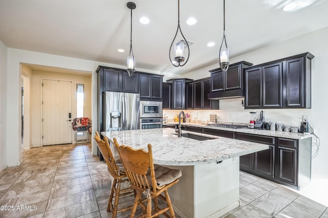 kitchen featuring sink, light stone counters, an island with sink, pendant lighting, and stainless steel appliances