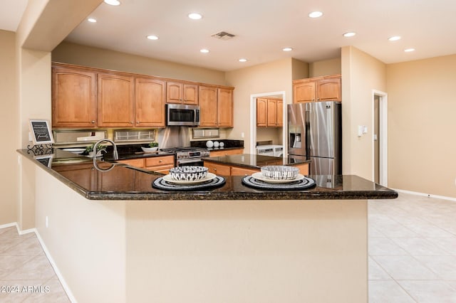 kitchen featuring appliances with stainless steel finishes, kitchen peninsula, light tile patterned floors, and dark stone countertops