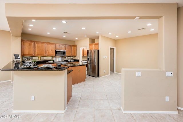 kitchen with light tile patterned floors, appliances with stainless steel finishes, kitchen peninsula, a kitchen island, and dark stone counters