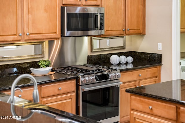 kitchen with appliances with stainless steel finishes, sink, and dark stone counters