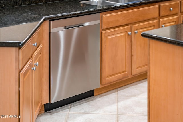 kitchen featuring stainless steel dishwasher, dark stone counters, and light tile patterned floors