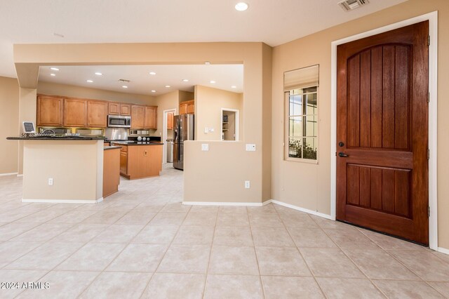 kitchen with light tile patterned flooring, appliances with stainless steel finishes, a kitchen island, and dark stone counters