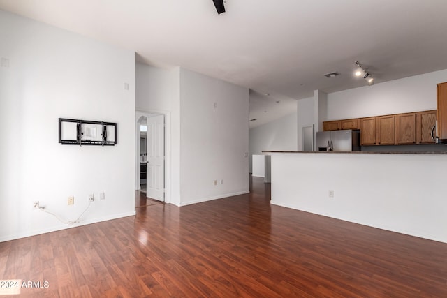 unfurnished living room with track lighting, dark wood-type flooring, and a high ceiling