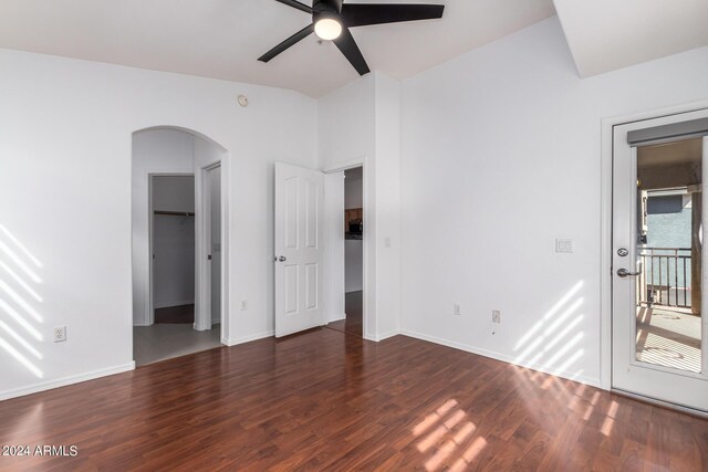 unfurnished bedroom with multiple windows, arched walkways, wood finished floors, and a walk in closet