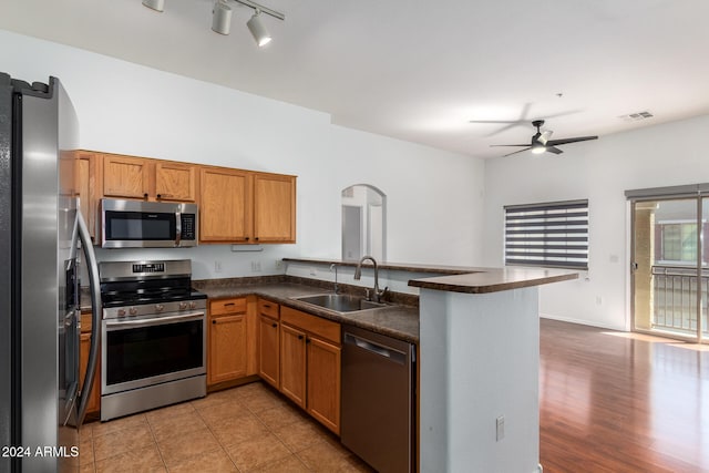 kitchen with appliances with stainless steel finishes, kitchen peninsula, light hardwood / wood-style flooring, ceiling fan, and sink