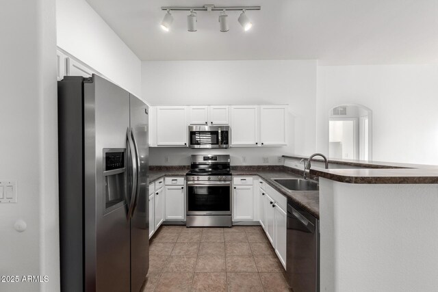 kitchen with light tile patterned floors, stainless steel appliances, a sink, dark countertops, and white cabinets
