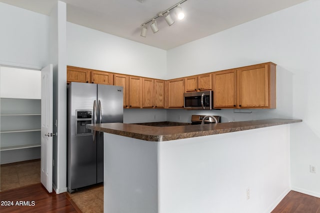 kitchen with appliances with stainless steel finishes, kitchen peninsula, track lighting, dark hardwood / wood-style floors, and sink