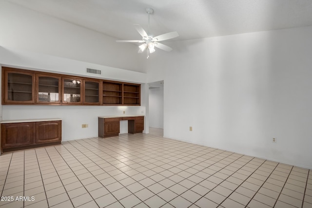 unfurnished living room with a towering ceiling, light tile patterned floors, built in desk, and ceiling fan